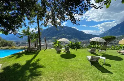 a lawn with chairs and umbrellas and a pool at Matailerhof in Tirolo