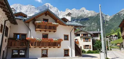 a building with flowers on the balconies in front of mountains at Chalet Stella Alpina in Val di Zoldo