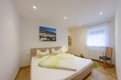 a bedroom with a white bed and a chair at Apartments Hubertus - central St Leonhard - free parking - Netflix - PasseiertalCard included - hiking and biking from doorstep in San Leonardo in Passiria