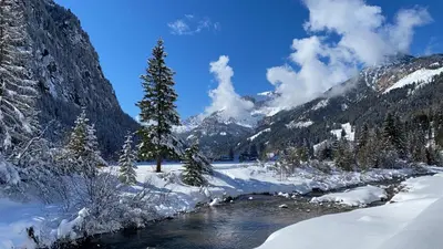 a river in the snow with mountains in the background at Calore di una Casa di Montagna in Campitello di Fassa