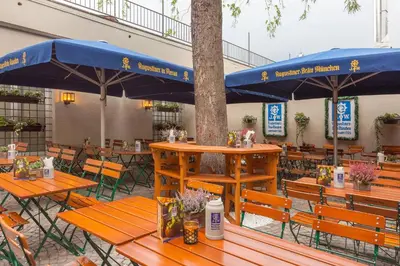 an outdoor restaurant with wooden tables and blue umbrellas at Augustiner in Meran in Merano