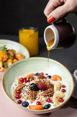 a person pouring syrup onto a bowl of cereal with fruit at Stay COOPER l Cooper apartments in Bolzano
