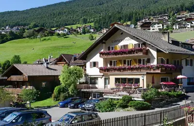 a large house with cars parked in a parking lot at Hotel Garni Vanadis in Ortisei