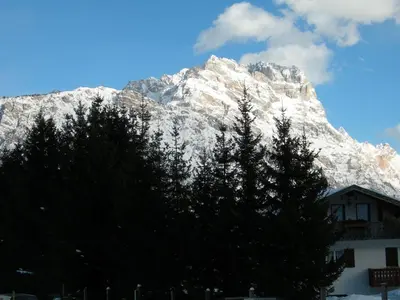 a snow covered mountain with trees in front of a building at Casa bianca in San Vito di Cadore