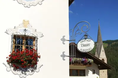 a building with a window with flowers and a sign at Gasthof/Albergo Dasser in San Martino in Badia
