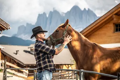 a man in a cowboy hat petting a horse at Gruberhof Coll in Funes