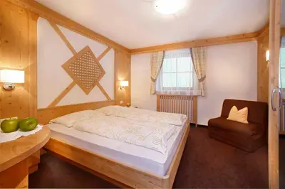 a bedroom with a large bed and a chair at Grohmann Apartments in Selva di Val Gardena