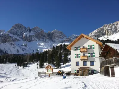 a building in the snow with mountains in the background at Rifugio Stella Alpina Spiz Piaz per escursionisti in Gardeccia - San Giovanni di Fassa