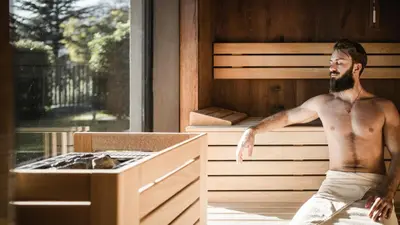 a man sitting in a sauna next to a bed at Vinea - Suites in Tirolo