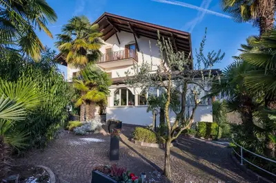 a house with palm trees in front of it at Hotel Weinberg in Appiano sulla Strada del Vino