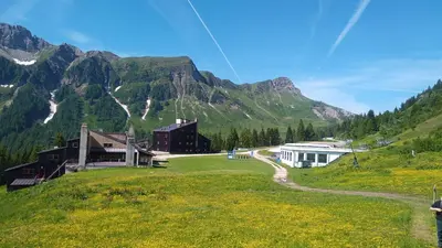 a building on a grassy hill in front of a mountain at IL COVO DELLO SCIATORE in Falcade