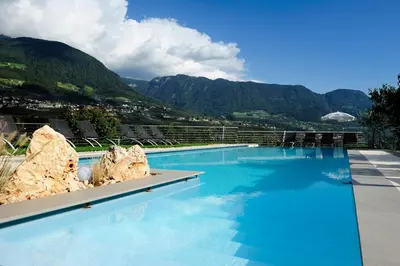 a large blue swimming pool with mountains in the background at Pension Schweigkofler in Tirolo