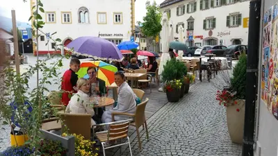 a group of people sitting at a table with umbrellas at Gasthof Traube in San Lorenzo di Sebato