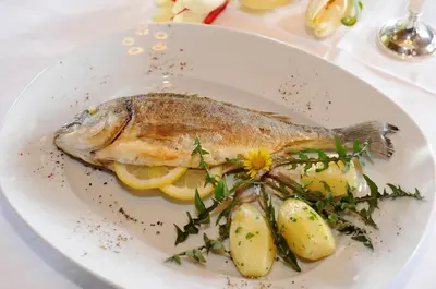 a plate with a fish and potatoes on a table at Hotel König Laurin in San Genesio Atesino