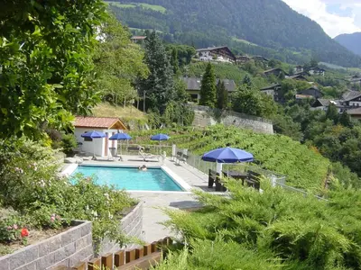 a swimming pool with umbrellas and a mountain at Appartement Tschivon in Schenna