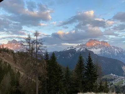 a view of a mountain range with trees and clouds at Dolomites Charme Chalet in Colle Santa Lucia