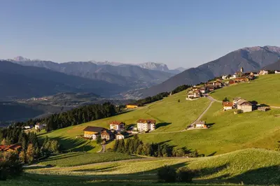 a village on a green hill with mountains in the background at Residence Speckerhof in Maranza