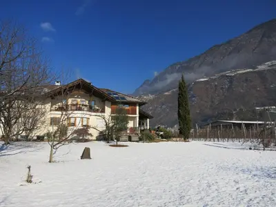 a house in a snowy field in front of a mountain at Feldererhof in Postal