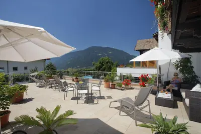 a patio with chairs and umbrellas with a mountain in the background at Garni-Hotel Tritscherhof in Tirolo