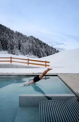 a person laying in a swimming pool in the snow at Hotel Pozzamanigoni in Selva di Val Gardena