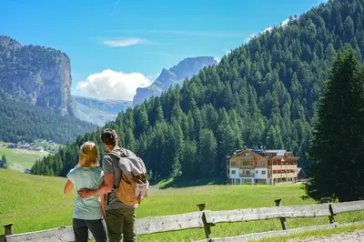 a man and woman standing on a fence looking at a mountain at Hotel Pozzamanigoni in Selva di Val Gardena