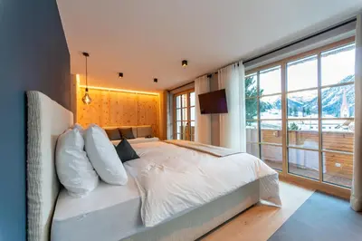a bedroom with a white bed with a large window at Penserhof - Alpine Hotel & Restaurant in Sarntal