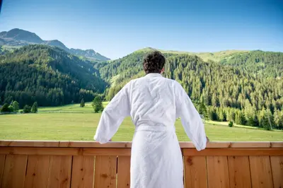 a woman in a white robe standing on a fence looking out at mountains at Penserhof - Alpine Hotel & Restaurant in Sarntal