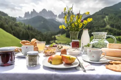 a table with food and drinks on it with mountains in the background at Unterkantiolerhof in Funes