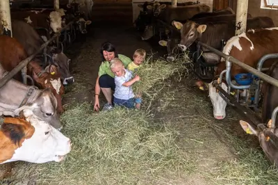 a woman and two children eating hay in a barn with cows at Unterkantiolerhof in Funes