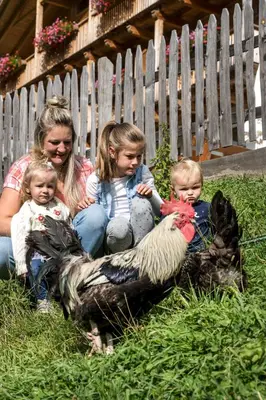 a woman and two children and a chicken in the grass at Unterkantiolerhof in Funes