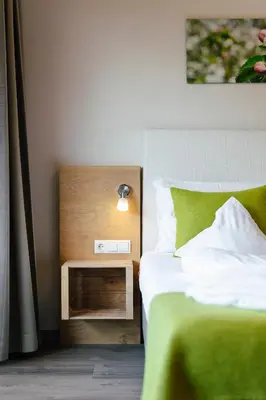 a bedroom with a bed with a green blanket and a night stand at Hotel Pfeiss in Lana
