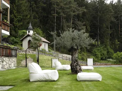 a group of white chairs and a tree in a yard at Golfhotel Sonne in Siusi