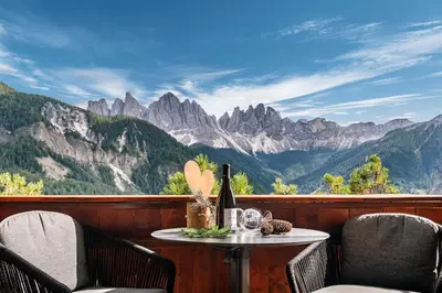 a table with a bottle of wine on a balcony with mountains at Schopplhof - panoramic apartments dolomites in Villnoss