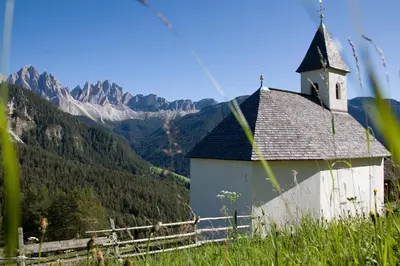a church on a hill with mountains in the background at Schopplhof - panoramic apartments dolomites in Villnoss