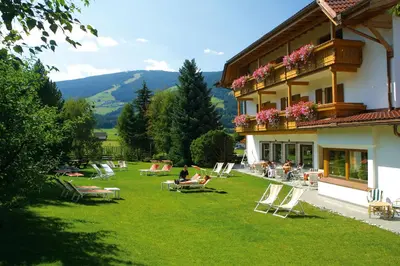 a group of people sitting on the lawn outside of a building at Hotel Markushof 3***S in Valdaora