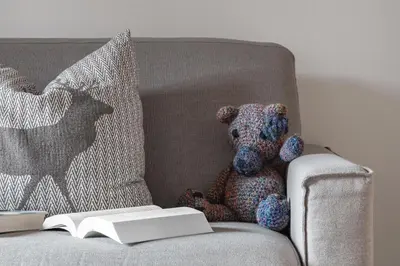 a teddy bear sitting on a couch with a book at Chalet Ciasa Tino & Sara - BelaVal Apartments in Corvara in Badia