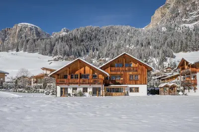 a log home in the snow with mountains in the background at Chalet Ciasa Tino & Sara - BelaVal Apartments in Corvara in Badia