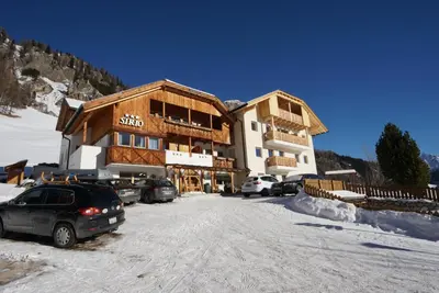 a large building with cars parked in the snow at Garnì Sirio in Colfosco