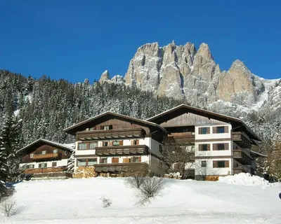 a building in the snow with a mountain in the background at Residence La Zondra in Pozza di Fassa