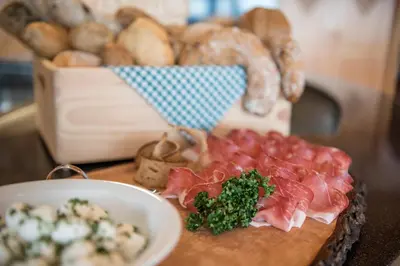 a table with a cutting board with meat and a basket of bread at Hotel Schönblick in Maranza