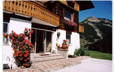 a house with flowers and a dog in front of it at Garni Martlhof in Selva di Val Gardena