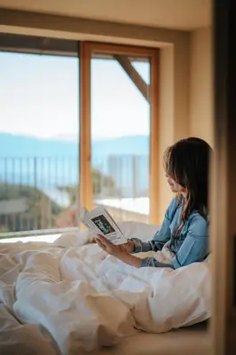 a woman sitting in bed reading a book at Hotel am Hang in Soprabolzano