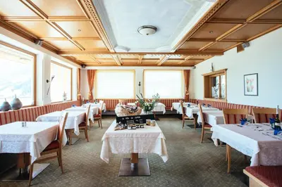 a restaurant with white tables and chairs and windows at Hotel Wildschütz in San Leonardo in Passiria