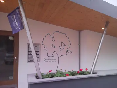 a sign in a building with a flag and flowers at B&B Casa Vanzetta in Ziano di Fiemme