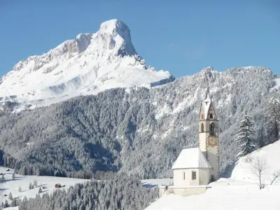 a church with a snow covered mountain in the background at Apartments Rit in La Valle