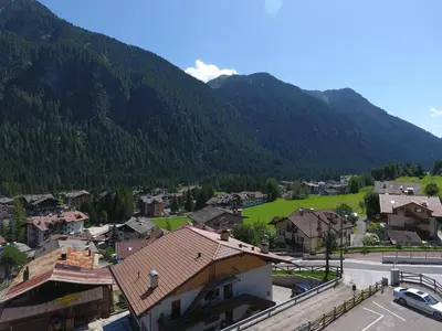 a village in the mountains with a green field at Hotel Stella Montis in Campitello di Fassa
