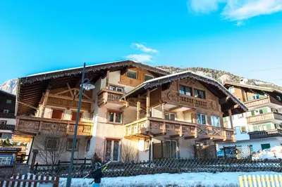 a large wooden building with snow in front of it at Appartamenti Ladina in Campitello di Fassa