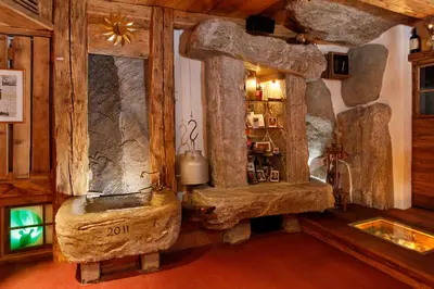 a living room with a rock fireplace in a log room at MENA Guesthouse in Marlengo