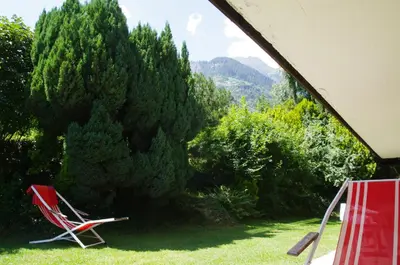 a red chair sitting in the grass in front of trees at Appartements Oberpefohl in Parcines