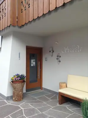 a porch with a door and a bench and flowers at Villa Seceda in Selva di Val Gardena